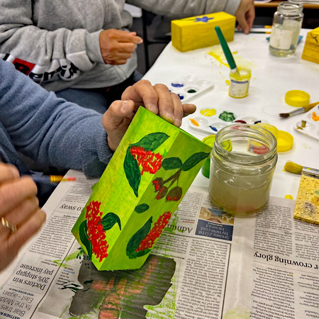 Bee hotel workshop creation in progress. The bee hotel is painted light green with bright red flowers and dark green foliage.